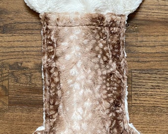 May include: A brown and white faux fur bone-shaped Christmas stocking with a white plush top and a loop for hanging.