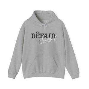 May include: A light gray hoodie with a drawstring hood and a kangaroo pocket. The front features the text "DÊFAID Livestock" in a distressed font, with a graphic of a sheep. A casual, comfortable garment.