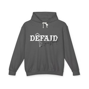 May include: A dark gray hoodie with a drawstring hood. The front of the hoodie features the white text "DÊFAID Livestock" in a bold, stylized font. The word "Livestock" is in a cursive font, with a small illustration of a goat.