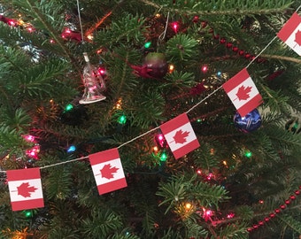 Pode incluir: Uma árvore de Natal decorada com bandeiras canadenses vermelhas e brancas, luzes de Natal vermelhas e brancas e um enfeite de vidro transparente.