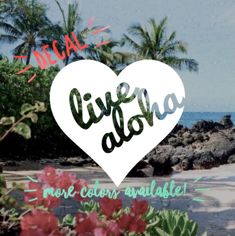 Op de afbeelding: Een witte hartvormige sticker met de woorden "live aloha" in een scriptlettertype. De sticker is geplaatst tegen een achtergrond van een tropische strandsc&egrave;ne met palmbomen, oceaan en bloemen. Tekst bovenaan luidt "DECAL" en onderaan "more colors available!"