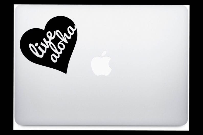 Op de afbeelding: Een zwarte hartvormige sticker met de woorden "live aloha" in witte letters is bevestigd op een zilveren laptop. Het Apple-logo is zichtbaar.