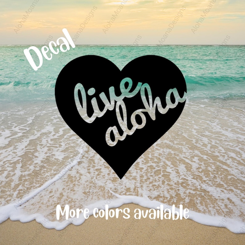 Op de afbeelding: Een zwarte hartvormige sticker met de woorden "live aloha" in een cursief lettertype. De achtergrond toont een strandsc&egrave;ne met oceaangolven en de tekst "Meer kleuren beschikbaar". Het woord "Decal" staat ook in de afbeelding.