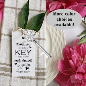 May include: A white card with black text that reads "thank you for being a key part of our past, present & future" with a silver key bottle opener attached. The card also includes the names "Shawn & Melissa" and the date "08.27.2022".