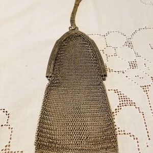 May include: A silver mesh purse with a chain strap. The purse has a scalloped bottom and a decorative top.