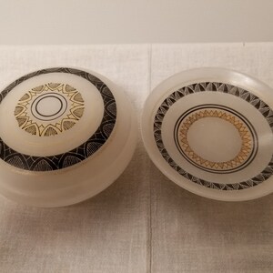 May include: Two frosted glass ceiling light covers with black and gold geometric designs. The larger cover has a larger circle in the center, while the smaller cover has a smaller circle in the center.