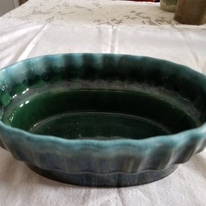 May include: A green and blue oval ceramic planter with a wavy rim. The planter is glazed and has a dark green interior.