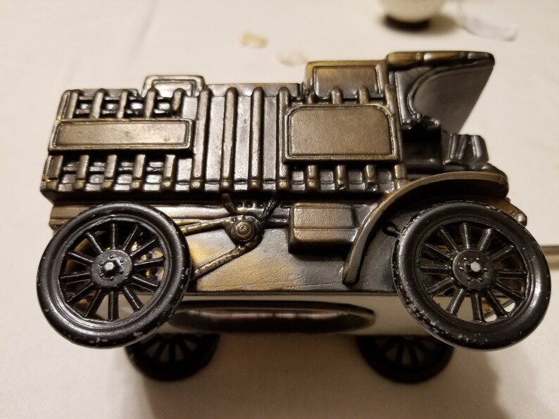 Peut inclure: Figurine de voiture ancienne de couleur bronze avec des roues noires. Le mod&egrave;le d&eacute;taill&eacute; comprend un radiateur, des phares et un capot incurv&eacute;. La voiture est un objet d&eacute;coratif, probablement un objet de collection ou un ornement de bureau.