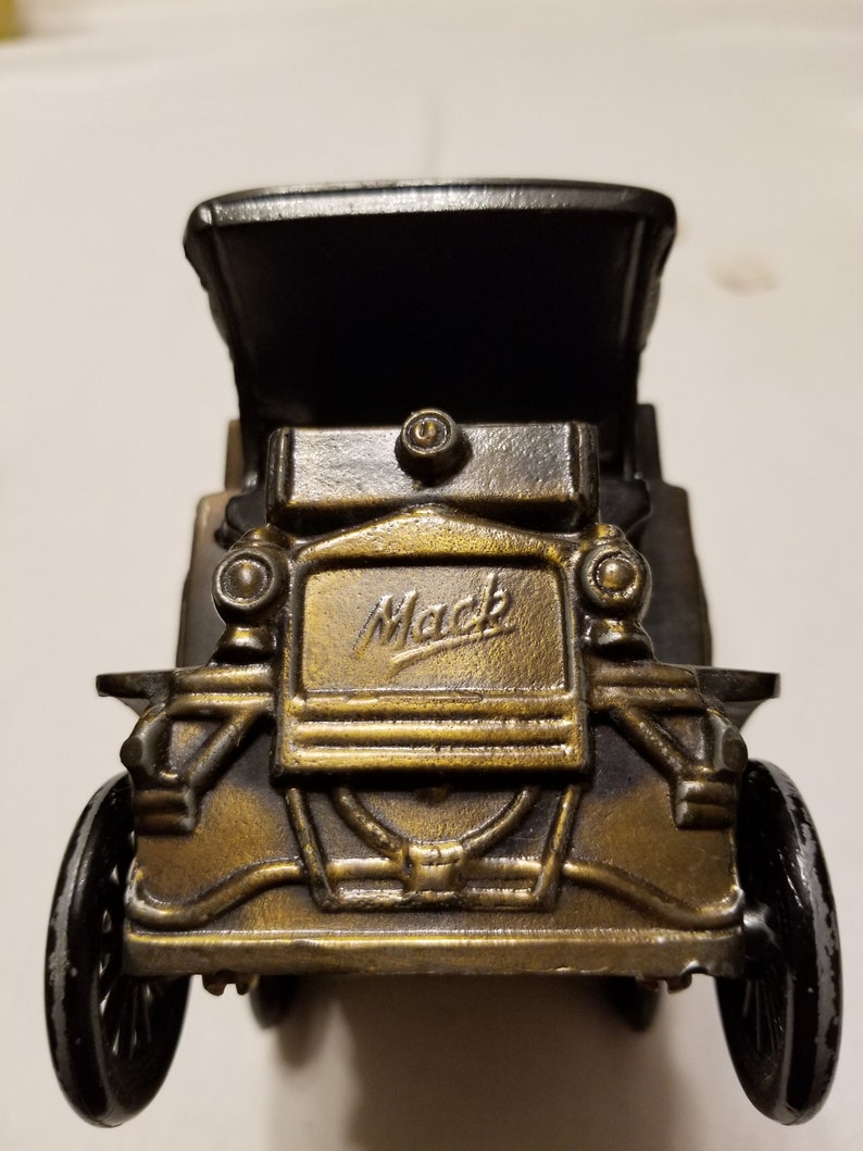 Peut inclure: Mod&egrave;le de voiture ancienne de couleur bronze avec le mot "Mack" en &eacute;criture sur le devant. La voiture a des roues noires et un toit noir. Le mod&egrave;le est une r&eacute;plique d&eacute;taill&eacute;e d'un v&eacute;hicule vintage.