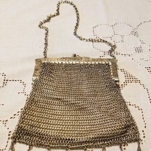 May include: A silver mesh purse with a chain strap and a fringe of silver beads. The purse is closed and has a decorative clasp.