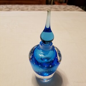 May include: A blue glass bottle with a clear glass stopper and a textured surface. The bottle has a round body and a pointed top.