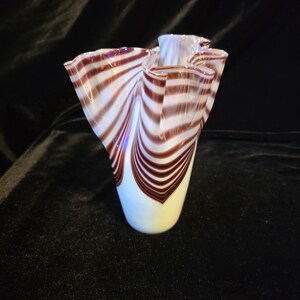 May include: A glass vase featuring a white base that transitions into a flared, ruffled rim. The body is decorated with swirling, dark brown stripes that create a rhythmic, wave-like pattern extending from the narrow bottom to the wide top.