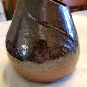 May include: A dark brown ceramic vase with a textured, speckled glaze. The vase has a wide opening and a rounded, bulbous shape.