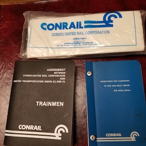 May include: Two black and blue Conrail train crew manuals. The front cover of the black manual says "Agreement between Consolidated Rail Corporation and United Transportation Union (C) and (T) Trainmen". The front cover of the blue manual says "Instructions for Completion of Time and Delay Report for Train Crews".