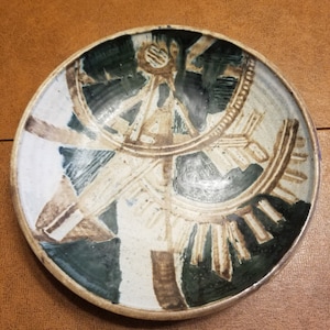 May include: A white ceramic bowl with a brown and green abstract design. The design features geometric shapes and lines.