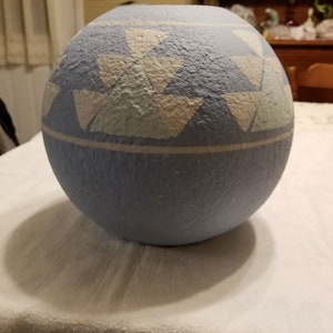 May include: A light blue ceramic vase with a white and light green geometric pattern. The vase is round and has a textured surface.