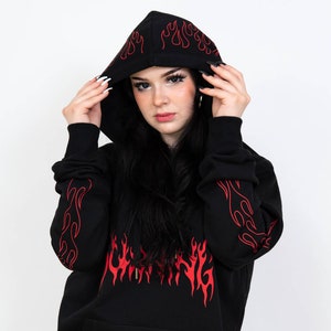 Puede incluir: Sudadera con capucha negra con un dise&ntilde;o de llamas rojas y la palabra "Burning" en llamas en la parte delantera. La sudadera tiene una capucha con cord&oacute;n y un bolsillo canguro.