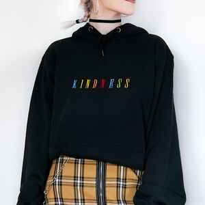 May include: Black hoodie with a rainbow colored "KINDNESS" embroidered on the front. The hoodie is paired with a yellow and black plaid skirt.