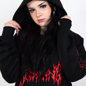 Puede incluir: Sudadera con capucha negra con estampado gr&aacute;fico de llamas rojas. La sudadera tiene un cord&oacute;n y un bolsillo canguro.
