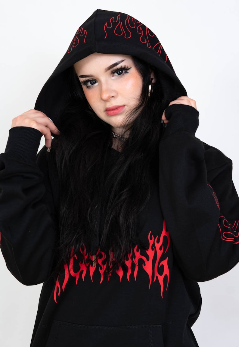 Puede incluir: Sudadera con capucha negra con estampado gr&aacute;fico de llamas rojas. La sudadera tiene un cord&oacute;n y un bolsillo canguro.