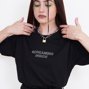 Pode incluir: Camiseta preta com texto branco que diz "SCREAMING INSIDE". A modelo est&aacute; usando um colar de corrente prateada com um cadeado dourado.