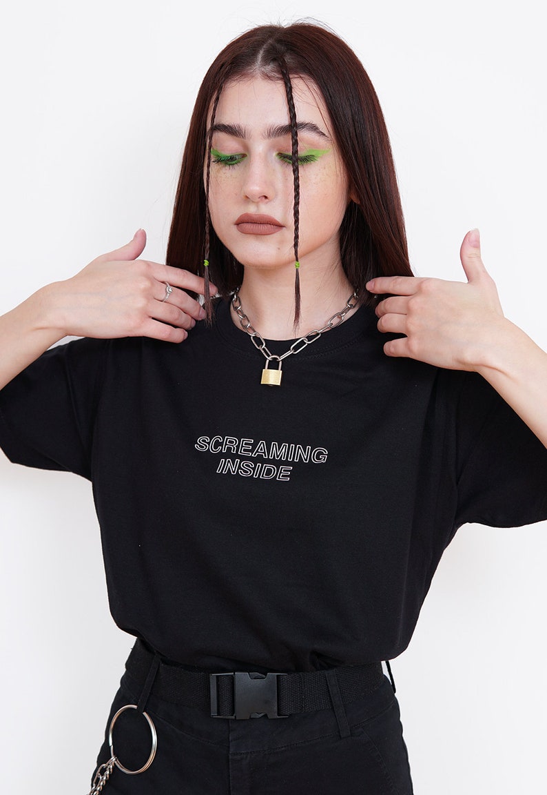 Pode incluir: Camiseta preta com texto branco que diz "SCREAMING INSIDE". A modelo est&aacute; usando um colar de corrente prateada com um cadeado dourado.