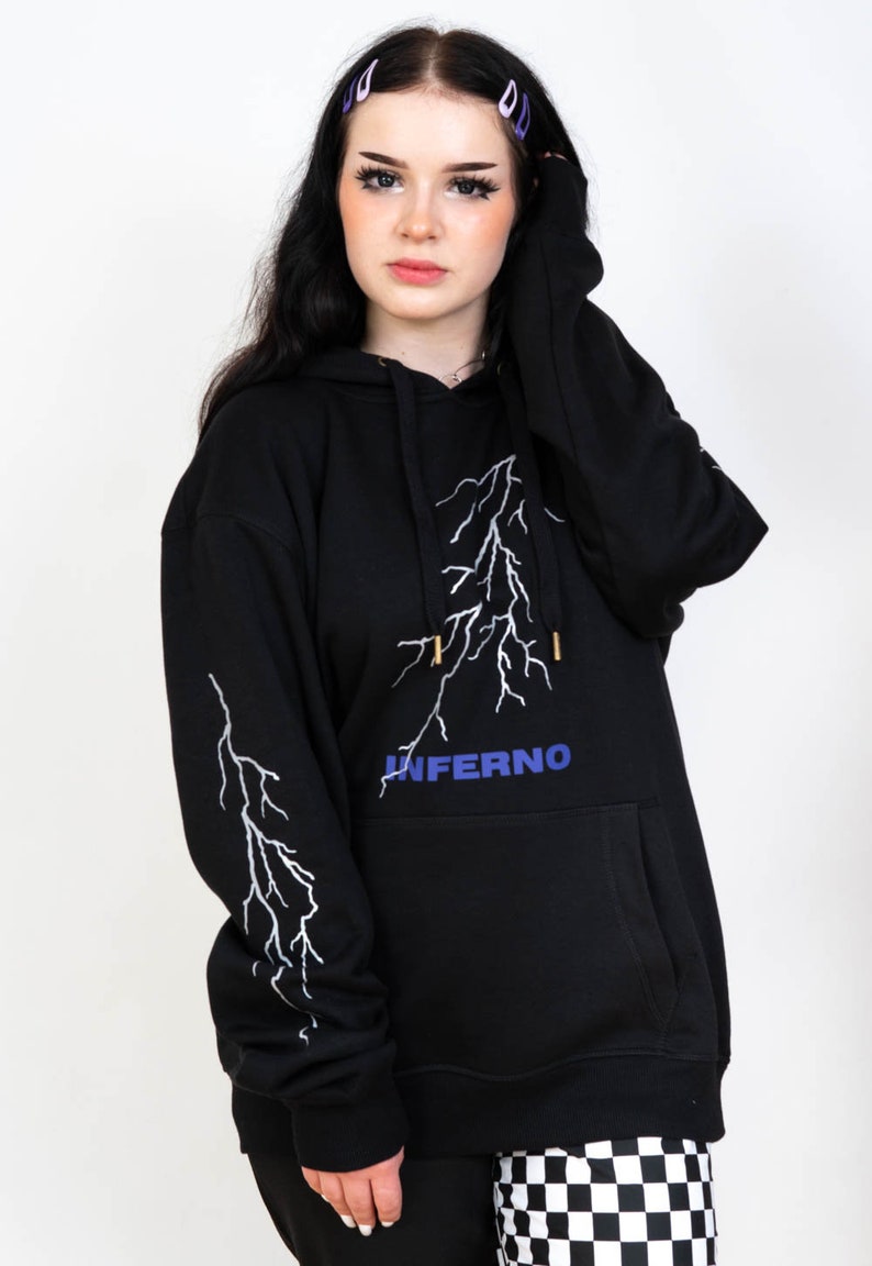 Puede incluir: Sudadera con capucha negra con un dise&ntilde;o de rayo blanco y la palabra "INFERNO" en letras azules.