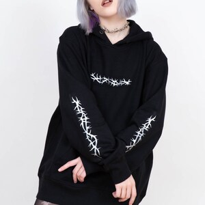 May include: Black oversized hoodie with silver barbed wire design on the sleeves and across the chest. The hoodie has a drawstring hood.