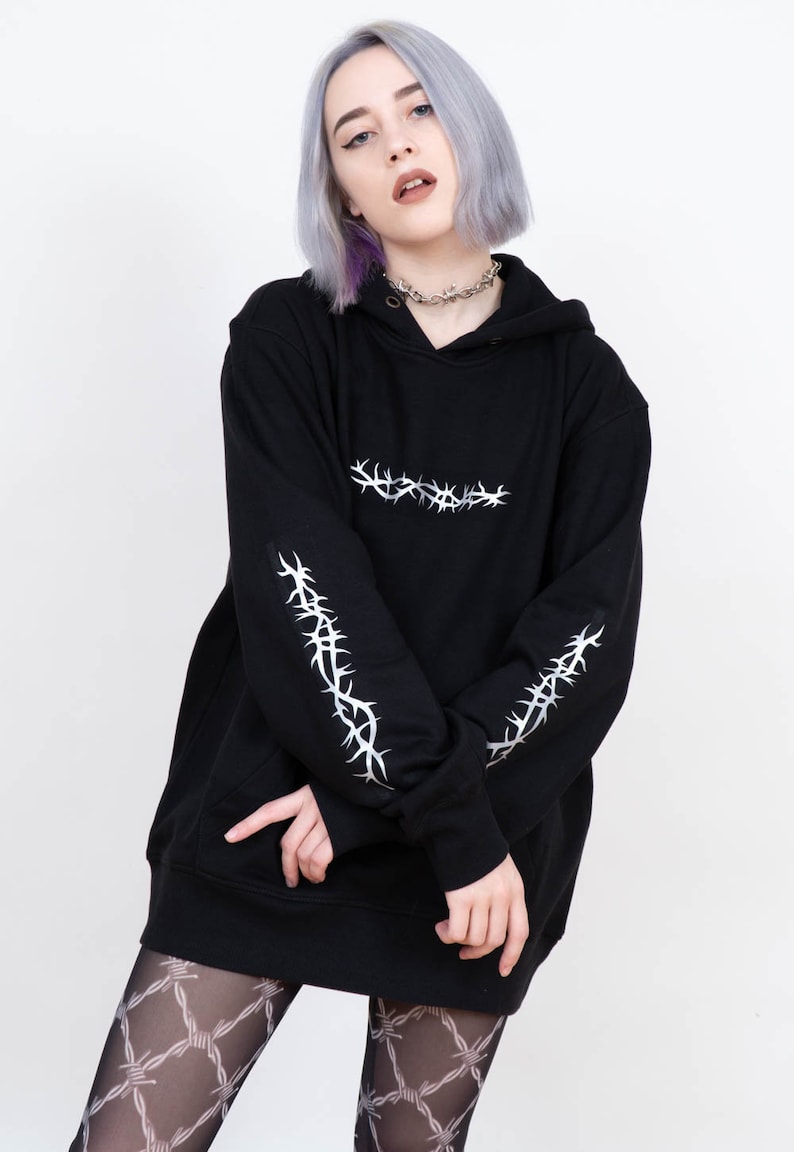 May include: Black oversized hoodie with silver barbed wire design on the sleeves and across the chest. The hoodie has a drawstring hood.
