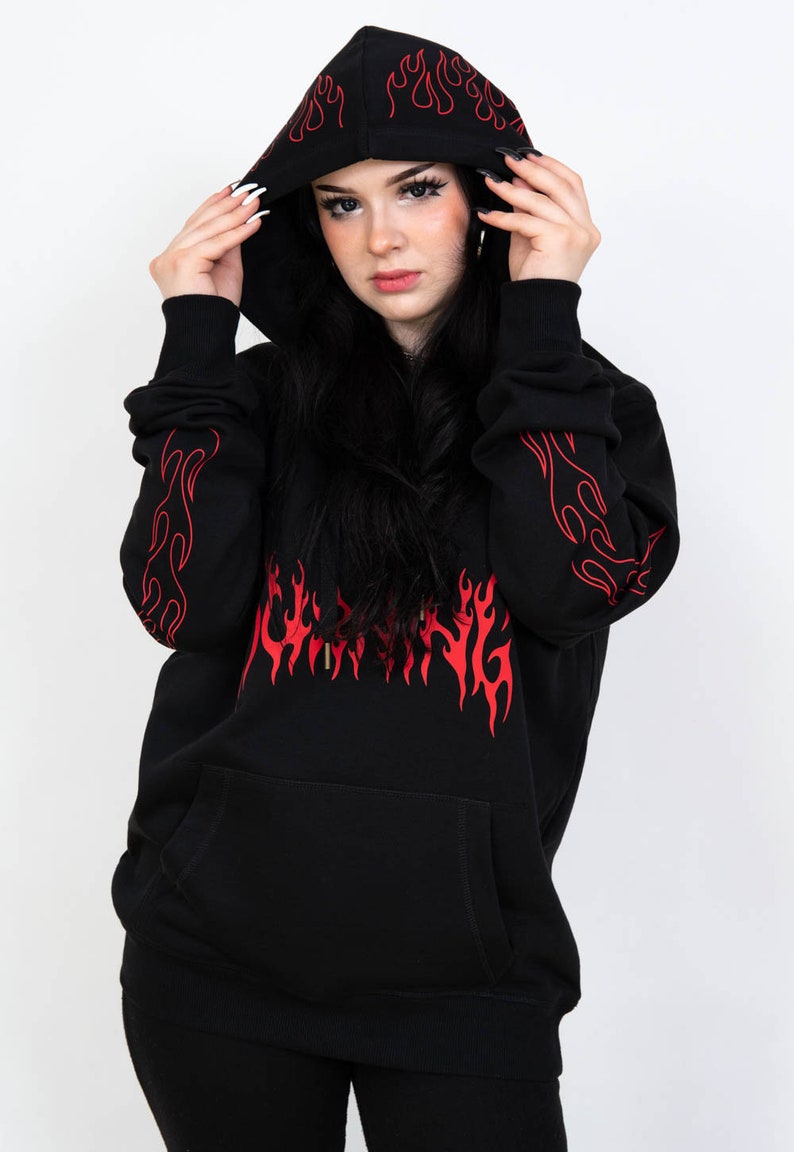 Puede incluir: Sudadera con capucha negra con un dise&ntilde;o de llamas rojas y la palabra "Burning" en llamas en la parte delantera. La sudadera tiene una capucha con cord&oacute;n y un bolsillo canguro.