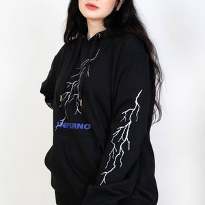Puede incluir: Sudadera con capucha negra con un dise&ntilde;o de rayo blanco y la palabra "INFERNO" en letras azules en la parte delantera.