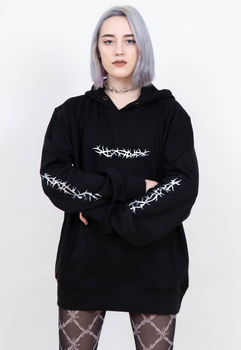 May include: Black oversized hoodie with silver barbed wire design on the sleeves and across the chest. The hoodie has a drawstring hood and a kangaroo pocket.