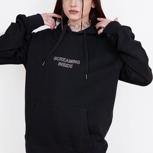 May include: Black hooded sweatshirt with the text "SCREAMING INSIDE" in white outlined lettering.