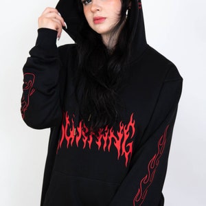 Puede incluir: Sudadera con capucha negra con un dise&ntilde;o de llamas rojas en la parte delantera y las mangas. El texto "BURNING" est&aacute; escrito en llamas rojas en la parte delantera de la sudadera.