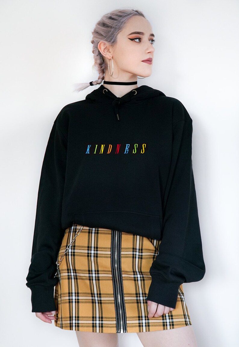 May include: Black hoodie with a rainbow colored "KINDNESS" embroidered on the front. The hoodie is paired with a yellow and black plaid skirt.