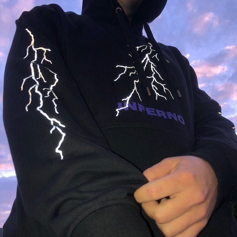 Puede incluir: Sudadera con capucha negra con un dise&ntilde;o de rayo reflectante y la palabra "INFERNO" impresa en morado en la parte delantera.