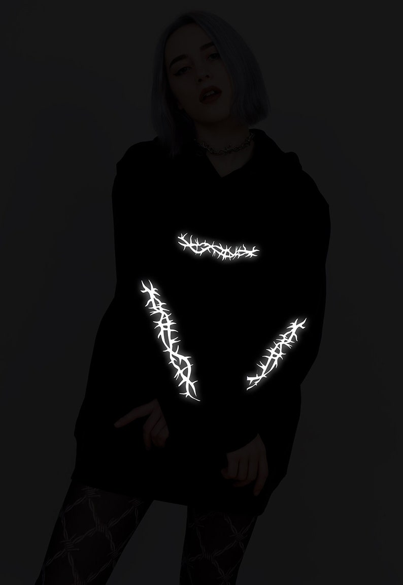 May include: Black hoodie with reflective white thorn designs on the sleeves and chest.