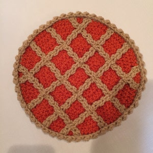 May include: A crocheted pie dish with a tan crust and an orange filling. The pie is made with a woven pattern.