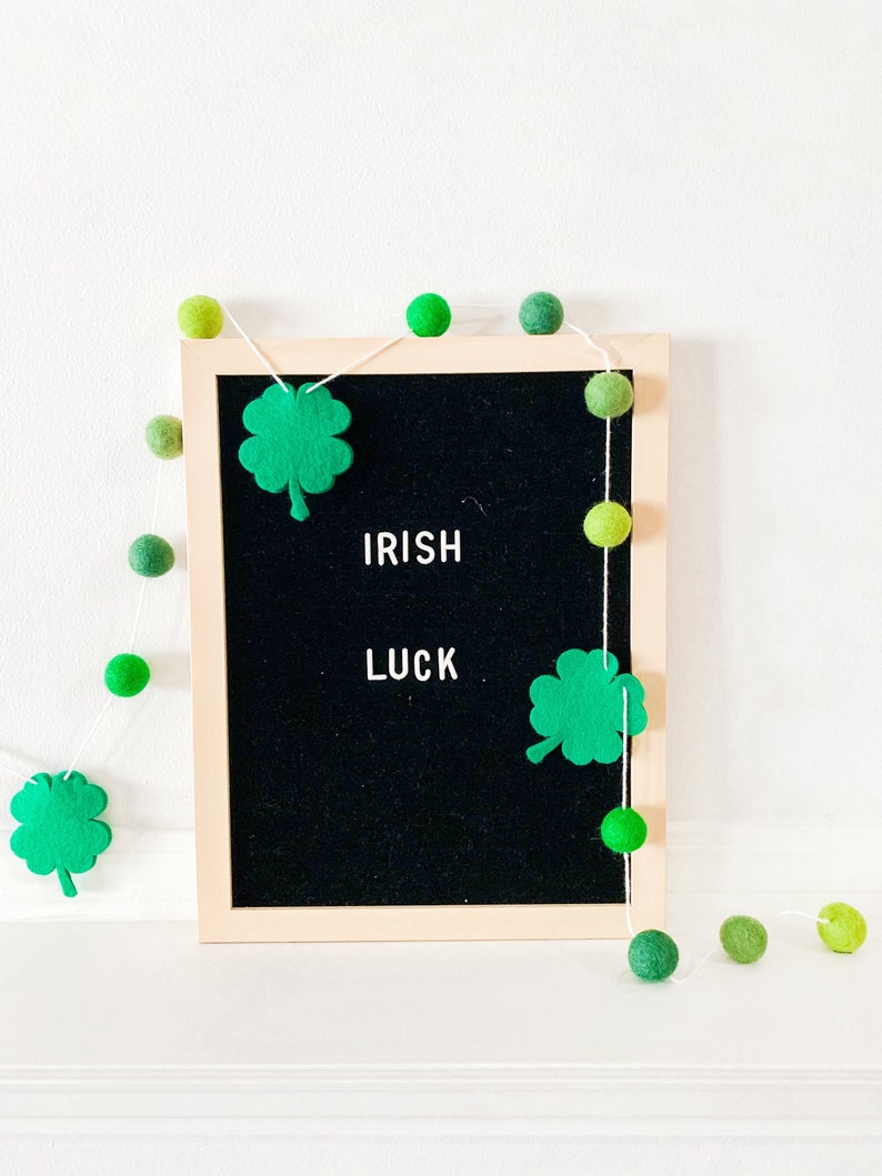 May include: A black letter board with the words "IRISH LUCK" spelled out in white letters. A green felt shamrock is on the left side of the board and another is on the right. A string of green felt balls is strung around the board.