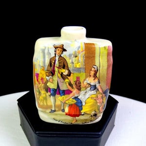 Op de afbeelding: Kleine, rechthoekige keramische fles met een gedetailleerde illustratie van een historische scène. De scène toont figuren in historische kleding, met de tekst "Cries of London - Miniature - Yellow Primrose". De fles is crèmekleurig.
