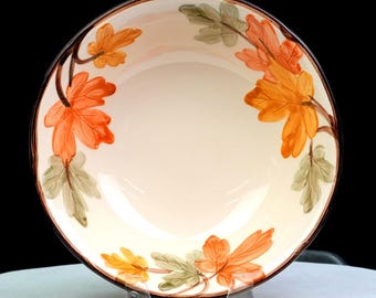 May include: A round ceramic bowl with a cream-coloured interior featuring a painted pattern of orange, yellow, and sage green maple leaves around the inner rim. The bowl has a dark brown rim and a smooth, glossy finish throughout the interior surface.
