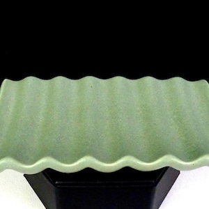 Peut inclure: Un plateau rectangulaire en céramique de couleur vert sauge doux présentant une texture de surface ondulée et cannelée distincte. Le plateau possède une finition mate uniforme sur toute sa surface supérieure, créant des crêtes parallèles.