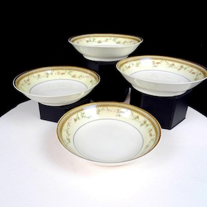May include: Four white porcelain bowls with a floral and gold rim design. The bowls are arranged on a white surface against a black background. The bowls are likely for serving soup or pasta.