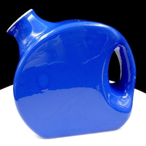 May include: A bright blue ceramic jug with a rounded form and a unique handle. The jug has a white rim and a glossy finish, offering a striking contrast. The design is modern and functional, suitable for serving.
