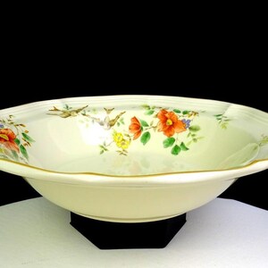 May include: Cream-colored, oval-shaped ceramic bowl with a floral design. The rim is scalloped and trimmed with gold. The floral pattern includes red, orange, and yellow flowers with green leaves. A decorative piece for serving.