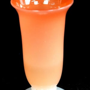 May include: A tall, slender vase made of frosted glass with a vibrant orange hue that transitions to a lighter, translucent peach tone towards the base. The vase features a wide, flared rim and sits securely on a solid, opaque white circular glass pedestal base.