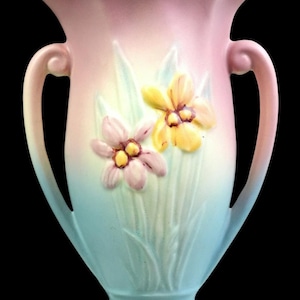 Può includere: Un vaso in ceramica caratterizzato da una sfumatura pastello che passa dal rosa in alto all'azzurro alla base. Il recipiente presenta due manici curvi e un bordo smerlato, decorato con motivi floreali in rilievo dipinti a mano in giallo e rosa.