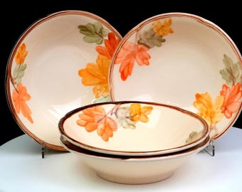 May include: Three cream-coloured ceramic bowls with scalloped edges and a brown rim. Each bowl features a hand-painted design of orange, yellow, and sage green autumn leaves. Two bowls are positioned upright in the back, while one sits in the front.