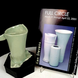 Puede incluir: Una jarra de cerámica de color verde claro con un borde acampanado y una sola asa, junto a un cartel de exposición rectangular titulado FULL CIRCLE, del 21 de marzo al 22 de abril de 2001, con Ken Stevens y Kittredge Gallery, University of Puget Sound.
