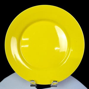 May include: A bright yellow ceramic plate with a glossy finish. The plate has a wide rim and a slightly recessed center. The plate is displayed against a black background.